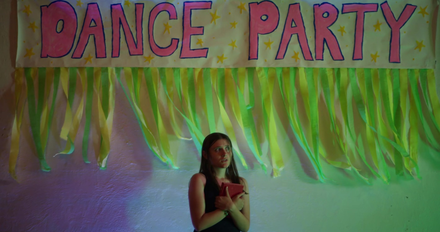 Olivia clutches her book under a hand-painted Dance Party banner.
