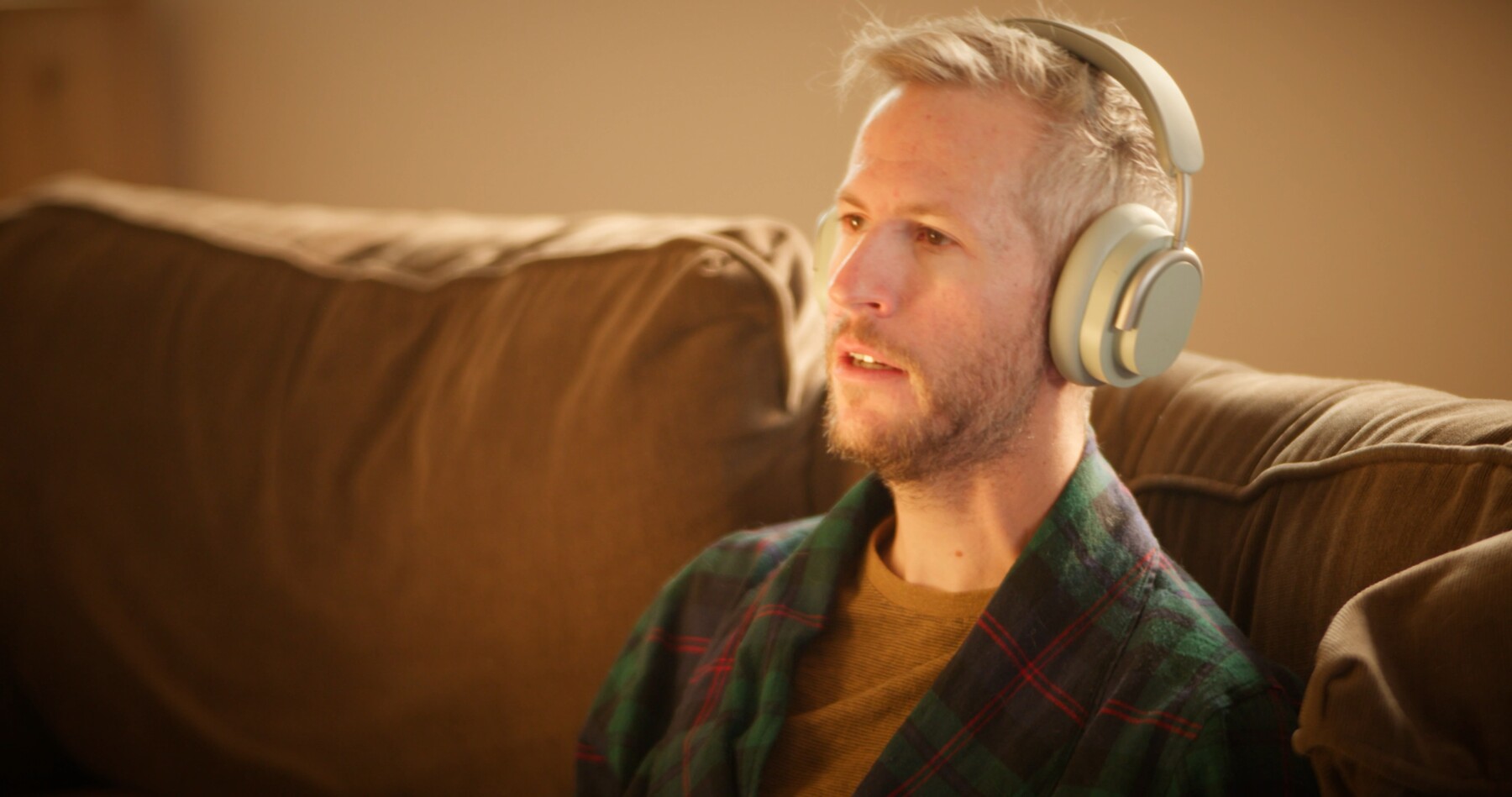 A man in headphones and a plaid robe talks on the couch.