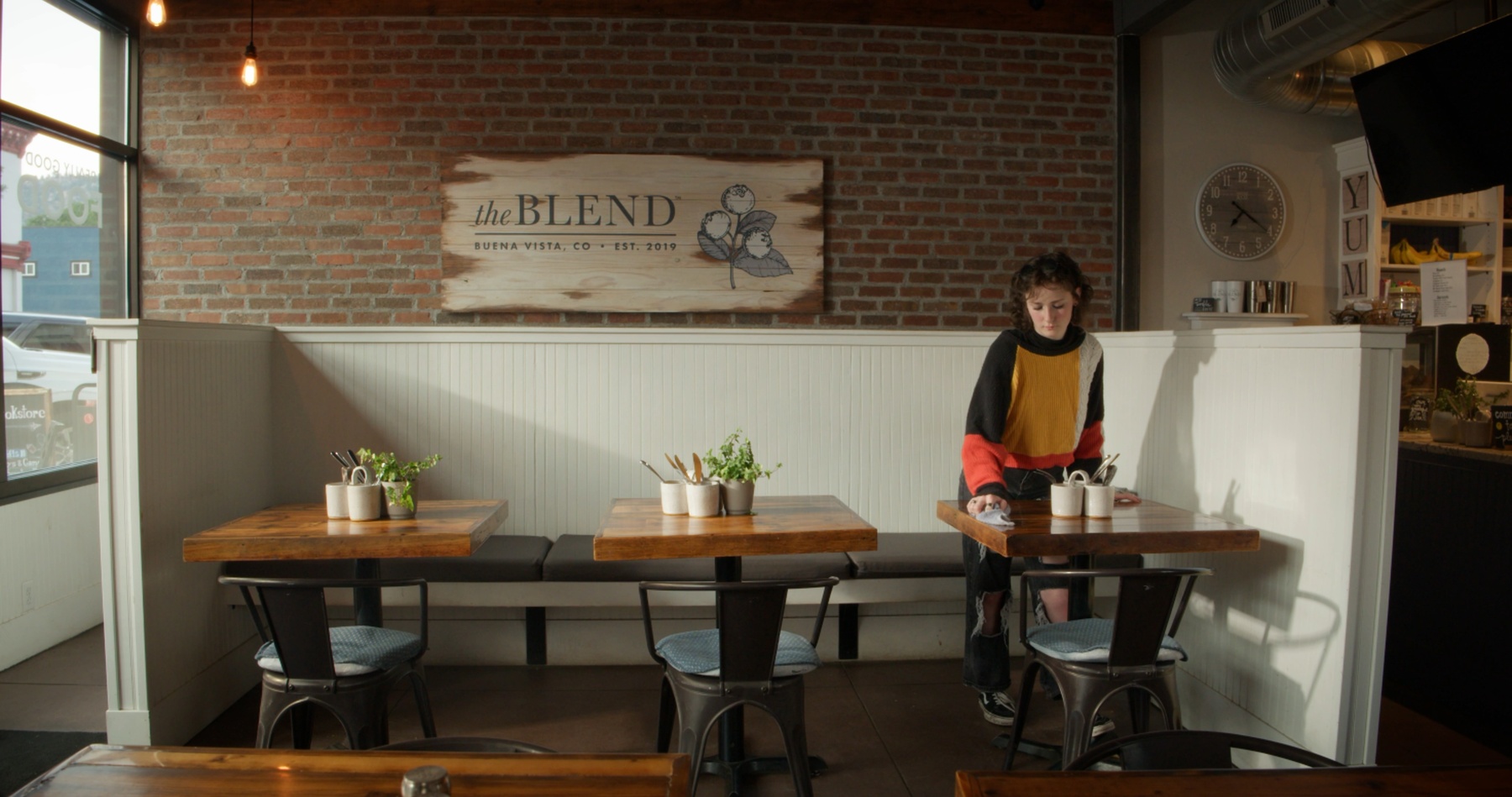 Maddy wipes down a table beneath the Blend's wooden sign.