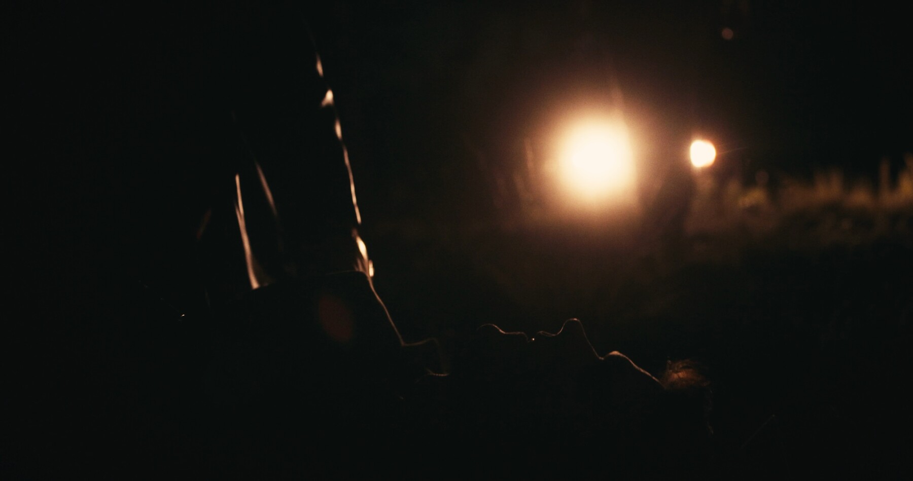Milo sits in silhouette against blurred lights, in the aftermath of being beaten.
