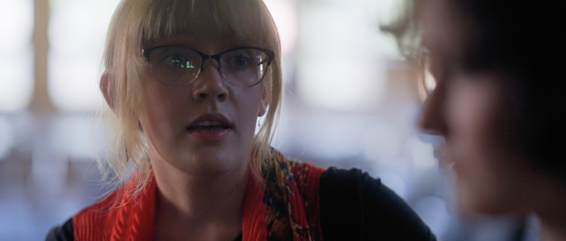 A woman wearing glasses and a red scarf speaks to Sadie.