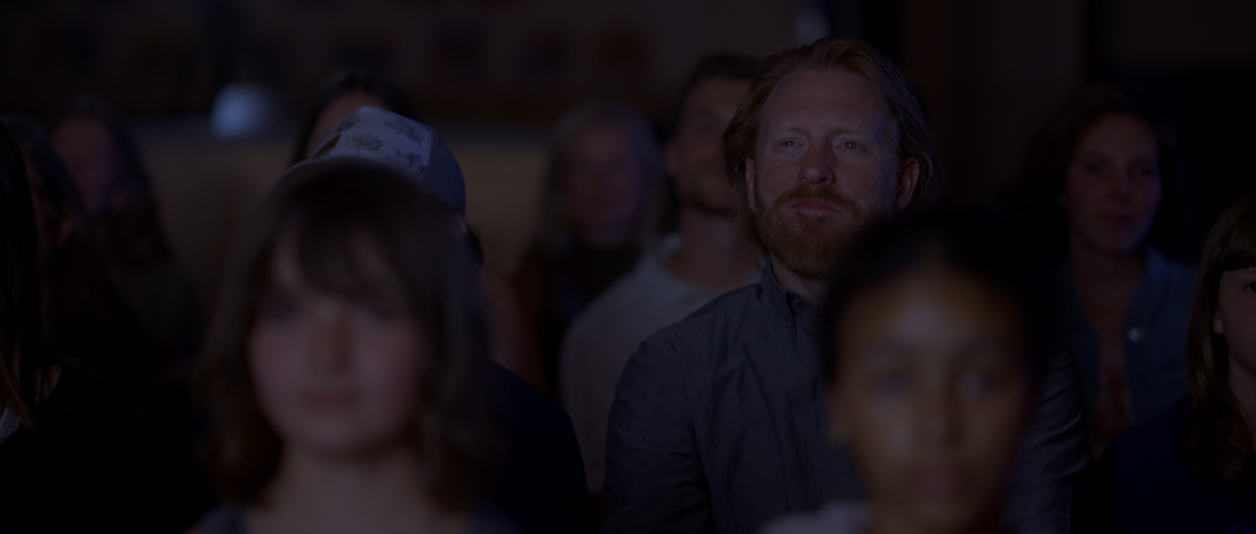 A man watches a performance from the audience in a darkened theater.